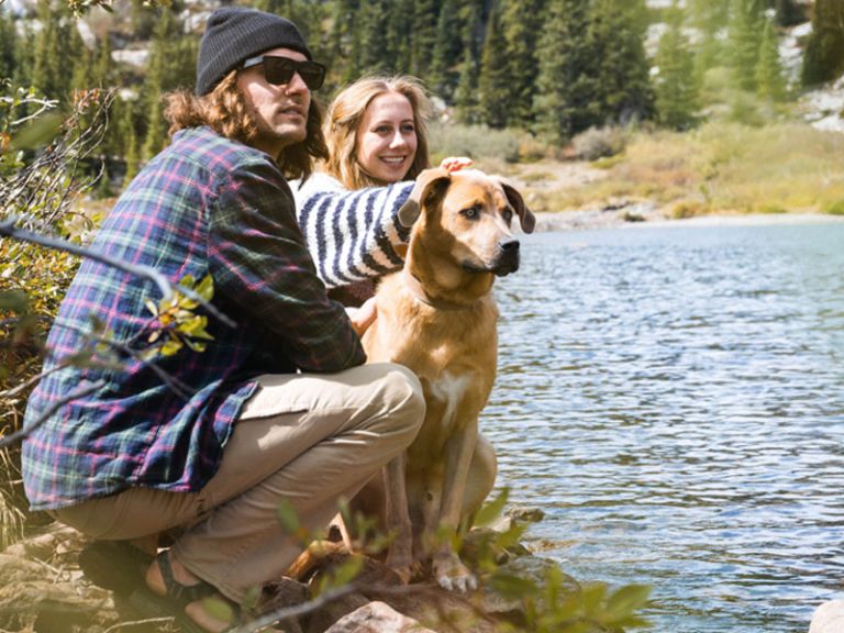 Eine Frau und ein Mann gehen mit ihrem Hund neben einem Fluss wandern